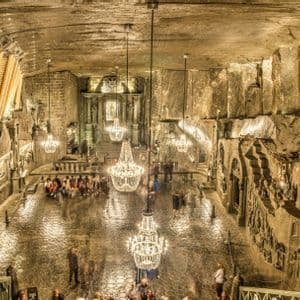 Una vasta sala sotterranea scavata nella roccia, illuminata da diversi grandi lampadari, mentre i visitatori camminano sul pavimento lucido.