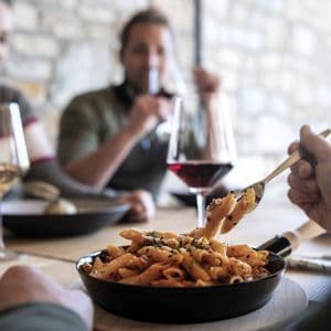 Mitglieder einer WeRoad-Gruppenreise genießen Penne-Pasta und Wein an einem rustikalen Restauranttisch.