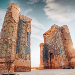 Due grandi e antiche torri in mattoni, adornate con elaborate piastrelle blu e turchesi, si ergono in una piazza sotto un cielo soleggiato.