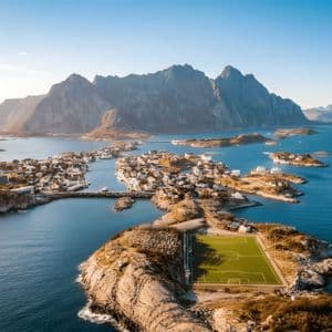 Una vista aerea di un campo da calcio su una penisola rocciosa accanto a un villaggio costiero circondato da isole e montagne.