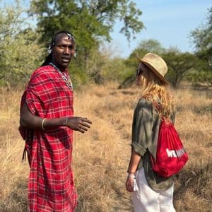 A Maasai man in traditional red attire talking to a woman from a WeRoad group trip in a grassy savanna.