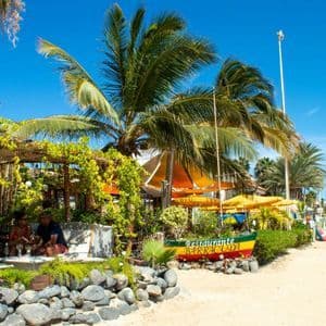 Eine WeRoad Gruppenreise auf einem Sandweg neben einem tropischen Strandrestaurant, umgeben von Palmen.