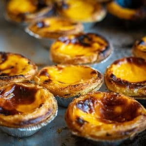 Primo piano di diverse pastéis de nata, crostatine portoghesi alla crema appena sfornate, su una teglia di metallo.