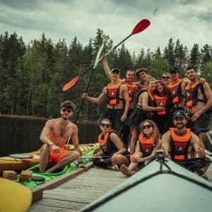 Eine WeRoad-Gruppe in orangefarbenen Schwimmwesten posiert mit ihren Kajaks für ein Foto auf einem Holzsteg.