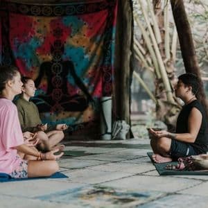 Un groupe WeRoad est assis en tailleur sur des tapis, méditant lors d'un cours de yoga dirigé par un instructeur.