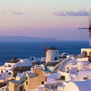 Case bianche e mulini tradizionali su una collina a picco sul mare, al tramonto colorato.