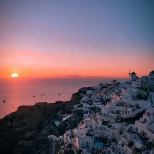 Un borgo di edifici bianchi arroccato su una scogliera a picco sull'oceano, al tramonto vivace.
