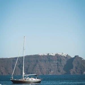 Una barca a vela con un gruppo WeRoad naviga sul mare blu di fronte a un'imponente scogliera con edifici bianchi in cima.
