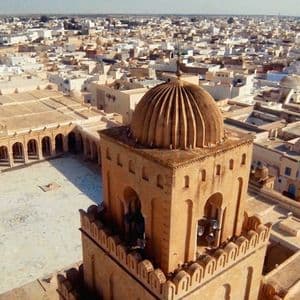 Vue aérienne du minaret à dôme et de la vaste cour d'une mosquée historique, avec un grand paysage urbain s'étendant jusqu'à l'horizon.