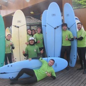 Un gruppo WeRoad in viaggio, con maglie verdi e mute abbinate, in posa con tavole da surf su un pontile di legno.