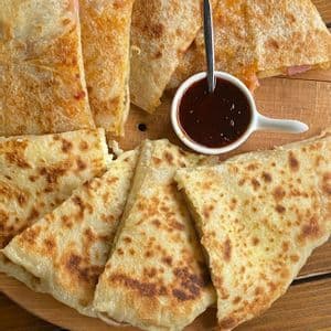 Quesadillas tostadas cortadas en triángulos y dispuestas en una tabla de madera con un pequeño tazón de salsa para mojar.