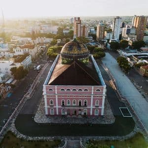 Aerial view of a grand, pink building with a colorful dome in the center of a city square at sunset.