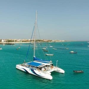 Un viaggio di gruppo WeRoad su un grande catamarano, che solca acque turchesi vicino a una costa costellata di numerose barche.