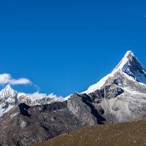 Una vetta aguzza e innevata si staglia contro un cielo azzurro e limpido, sopra colline rocciose e brulle.