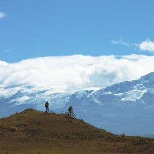 Sagome di un viaggio di gruppo WeRoad con mountain bike su una collina con lo sfondo di montagne innevate.