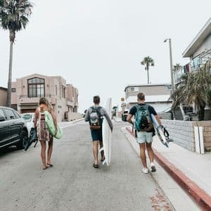 Un gruppo WeRoad di tre persone, viste di spalle, cammina per strada con le tavole da surf.