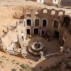 Una vista dall'alto di un'abitazione sotterranea circolare in terra, con cortile centrale, un pozzo e ingressi ad arco.