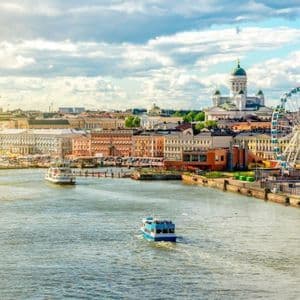 Una vista della città dall'acqua di un lungomare storico con una cattedrale, una ruota panoramica e diverse barche a vela.