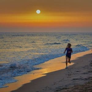 Una giovane donna in tenuta sportiva corre sulla sabbia bagnata in riva al mare durante un tramonto dorato.