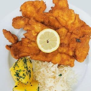 Schnitzel empanado con limón, arroz blanco y patatas a las finas hierbas.