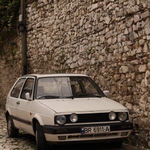 Un'auto bianca d'epoca parcheggiata su una strada acciottolata accanto a un alto muro di pietra rustico.