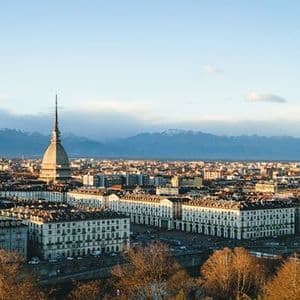 A dense cityscape featuring a prominent spire, with a distant snow-capped mountain range visible under a clear sky.