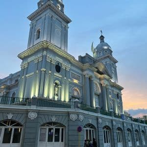 Una ornamentada catedral gris con dos torres está iluminada por focos bajo un cielo crepuscular.