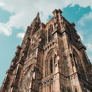 La facciata in pietra riccamente decorata di una cattedrale gotica, vista da un'angolazione bassa, sullo sfondo di un cielo azzurro con nuvole bianche.