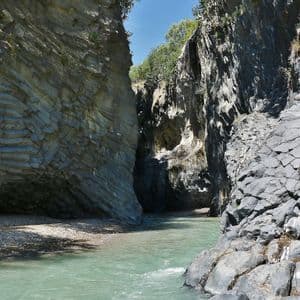 Un fiume dalle acque verde chiaro si snoda attraverso un canyon di roccia vulcanica stratificata e colonnare in una giornata di sole.