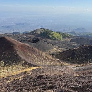 Un vasto paesaggio vulcanico con diversi crateri scuri e campi di lava che si affacciano su una città costiera in lontananza.