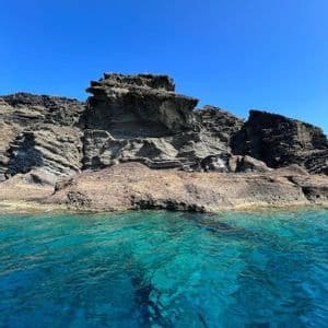 Una scogliera di roccia stratificata si erge da acque marine turchesi e limpide sotto un cielo blu luminoso e senza nuvole.