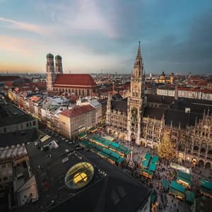 Una vista aerea di una piazza cittadina gremita di mercatini di Natale, circondata da edifici storici e un grande albero di Natale al tramonto.