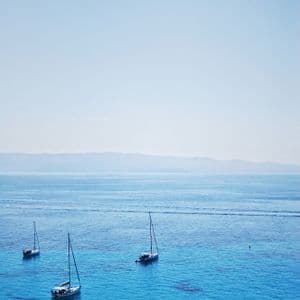 Trois voiliers flottent sur une eau calme et turquoise près d'un rivage lointain sous un ciel clair.
