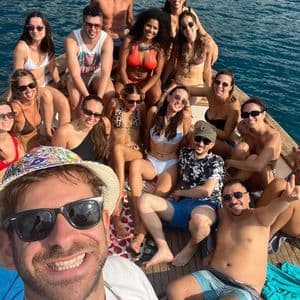 Un viaggio di gruppo WeRoad in costume da bagno, sorridenti per un selfie sul ponte di legno di una barca circondata da acqua blu.