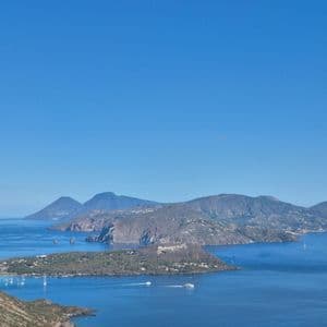 Una vista dall'alto di un arcipelago di isole montuose in un vasto mare blu, con diverse imbarcazioni sull'acqua sotto un cielo limpido.