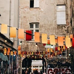 Des guirlandes de papier colorées et des guirlandes lumineuses traversent une étroite ruelle urbaine dont les vieux bâtiments ont des murs couverts de graffitis.