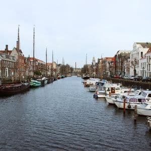 Barche e barche a vela sono ormeggiate lungo un canale cittadino fiancheggiato da tradizionali case in mattoni sotto un cielo grigio.