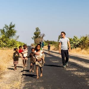 Un uomo di un viaggio di gruppo WeRoad cammina con un gruppo di bambini locali su una strada asfaltata in un paesaggio rurale e arido.