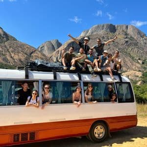 Un gruppo WeRoad in posa per una foto sul tetto e dai finestrini di un minibus, davanti a una catena montuosa rocciosa.