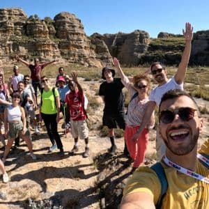 Un gruppo WeRoad si scatta un selfie durante un'escursione in un paesaggio roccioso e soleggiato, con tutti sorridenti e che salutano.
