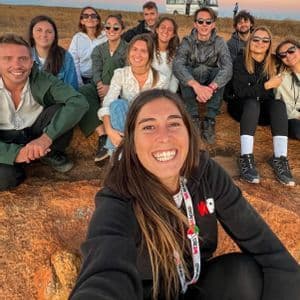 Una donna si scatta un selfie con il suo gruppo di viaggio WeRoad mentre sono seduti su uno sperone roccioso al tramonto.