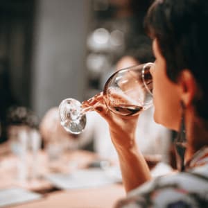 Una persona con capelli corti e scuri beve vino rosso da un bicchiere mentre è seduta a un tavolo durante un viaggio di gruppo WeRoad.