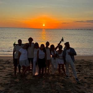 Un gruppo WeRoad posa su una spiaggia sabbiosa, stagliato contro un vibrante tramonto arancione sul mare.