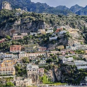 Una cittadina con edifici colorati è incastonata in una ripida scogliera verde, affacciata su una spiaggia con barche sull'acqua.