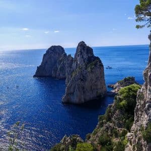 Due grandi faraglioni si ergono dal profondo oceano blu sotto un cielo sereno, visti da un'alta scogliera coperta di vegetazione.