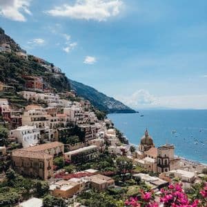 A high-angle view of a coastal village on a cliffside overlooking the sea, with vibrant pink flowers in the foreground.