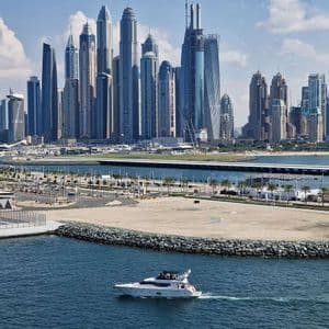 Un motoscafo bianco naviga su acque azzurre con un moderno skyline di numerosi grattacieli sullo sfondo.