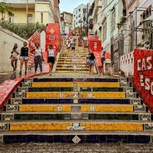 A WeRoad group trip poses on a long staircase decorated with colorful yellow, blue, and red mosaic tiles.