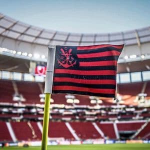 Primo piano di una bandierina d'angolo a strisce rosse e nere con lo stemma del Flamengo, su un campo da calcio, con i seggiolini dello stadio sfocati sullo sfondo.