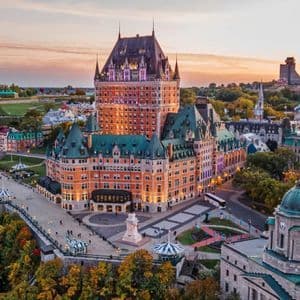 Vista aerea di un magnifico hotel-castello che si affaccia su una città e un fiume al tramonto, circondato da alberi autunnali.